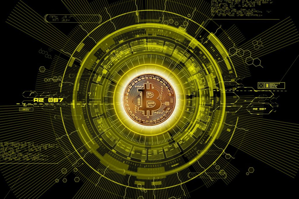 A digital illustration of a glowing Bitcoin symbol at the center of a futuristic, yellow and black interface. The design includes concentric circles, data lines, and hexagonal elements, representing digital technology and cryptocurrency networks.