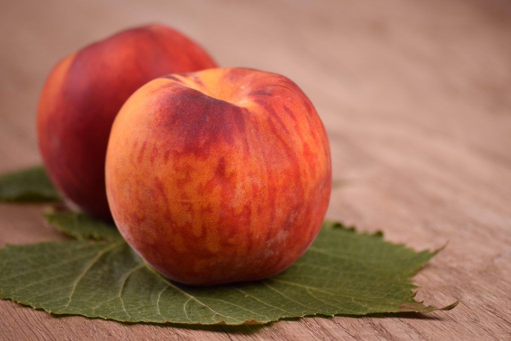 Ripe peach on green leaf on wooden surface.