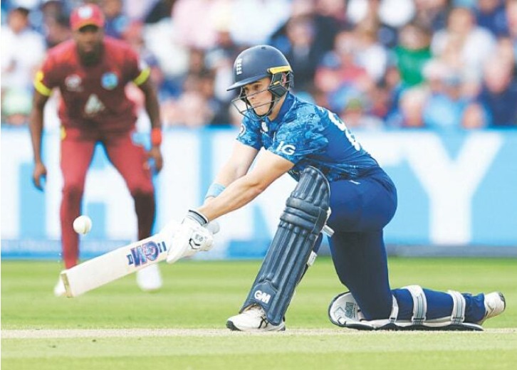 A cricket player in blue is batting, while another player in red fielding in the background.