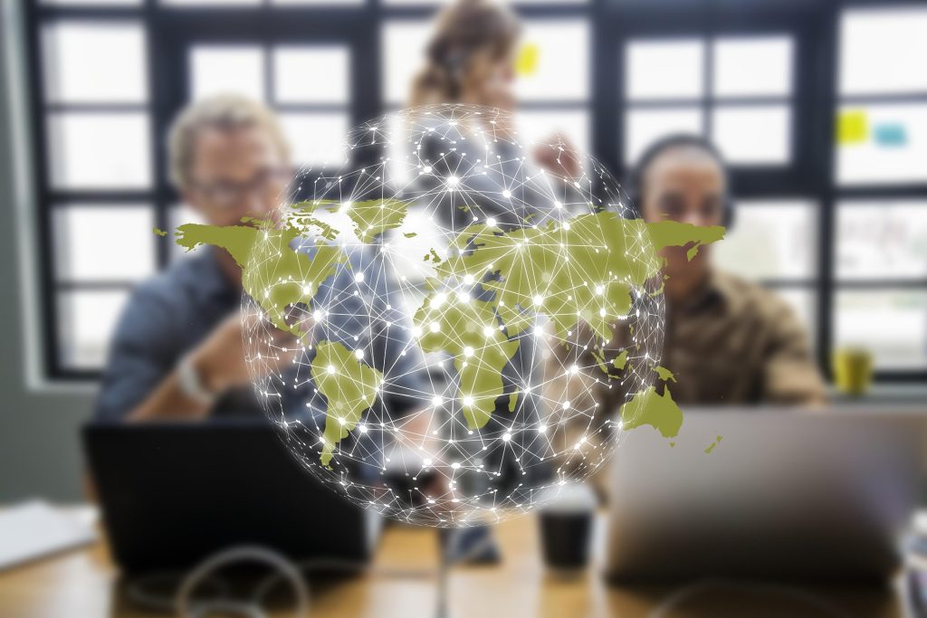 A group of people working together at a table with laptops, overlaid with a digital representation of a world map and network connections.