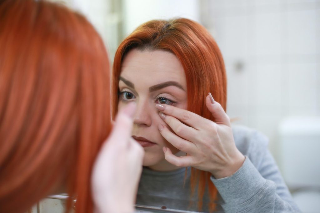 Woman applying a contact lens in front of a bathroom mirror