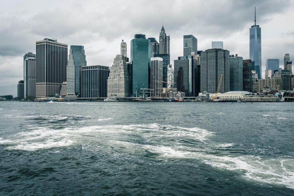 A waterfront view of a city skyline featuring tall modern buildings under a cloudy sky.
