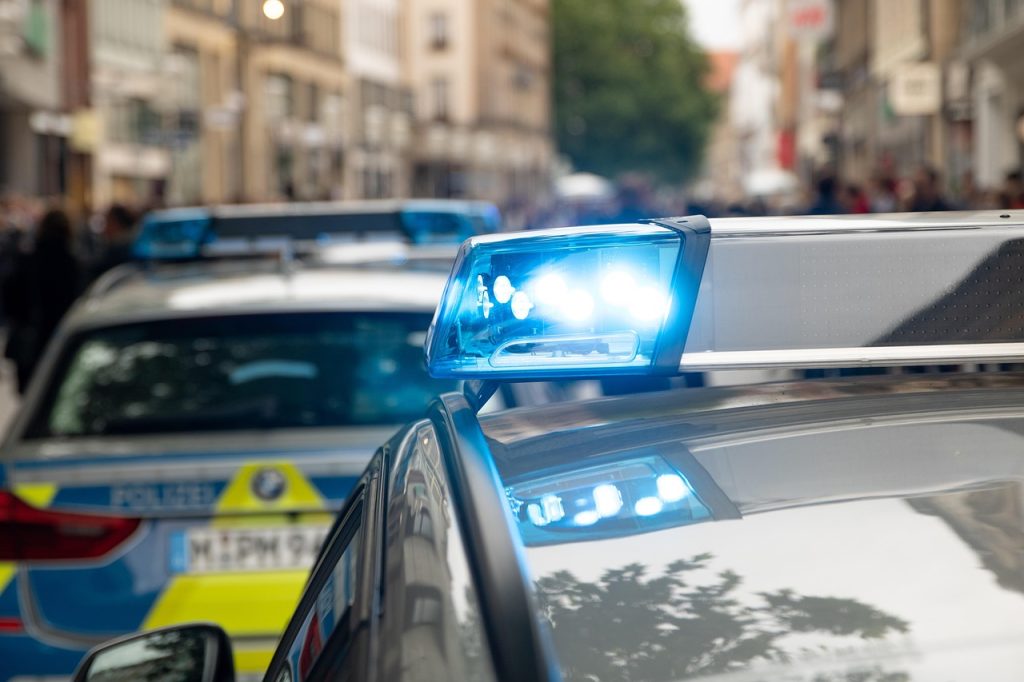 Close-up of a police car with flashing blue lights on a city street, with another police vehicle visible in the background.