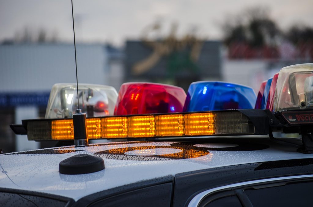 Close-up of a police car roof with flashing red, blue, and amber emergency lights, captured in a city setting during dusk.