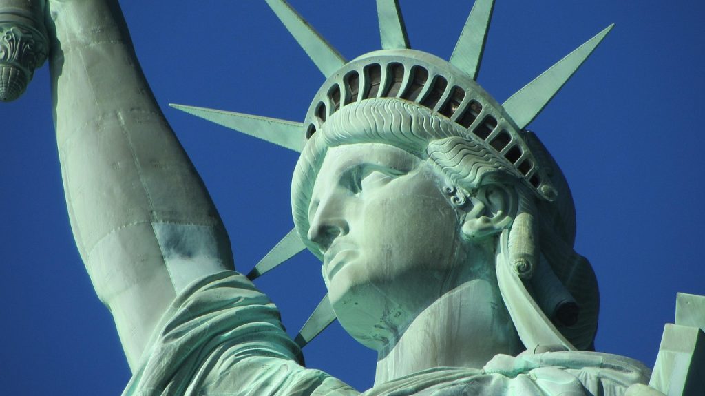 A close-up view of the Statue of Liberty's face and crown against a clear blue sky.

