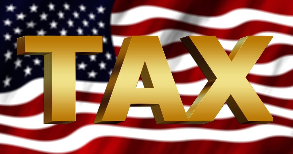 "The word 'TAX' in large gold 3D letters overlaid on an American flag background."