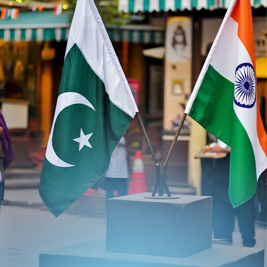 **Alt Text:** Pakistani and Indian flags side by side on a podium in an outdoor setting, symbolizing diplomacy.