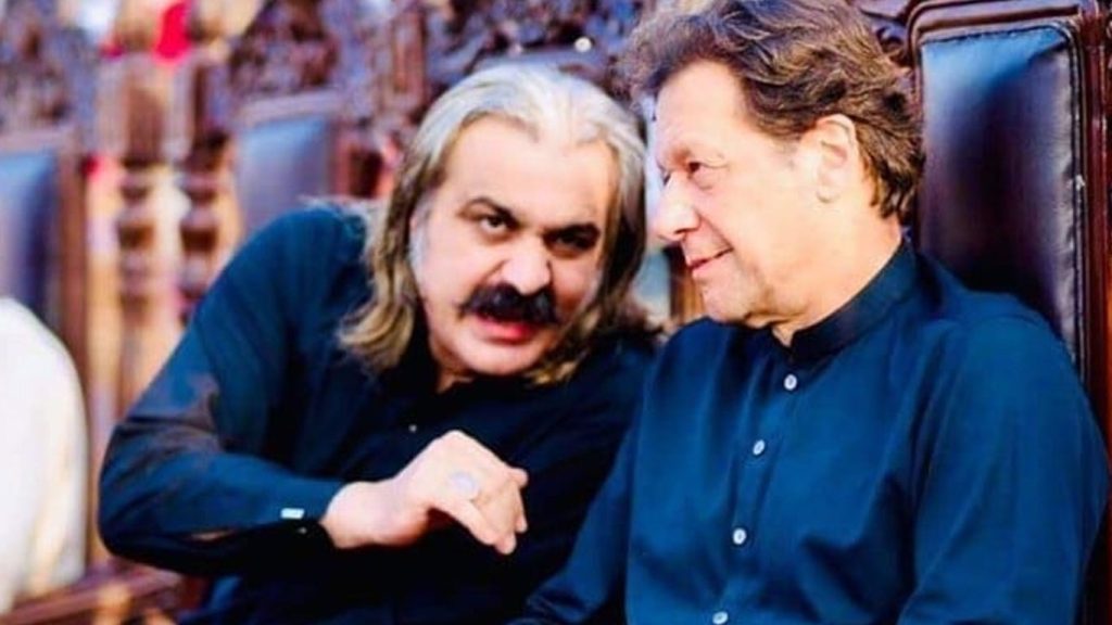 Ali amin and Imran Khan in traditional attire seated on ornate chairs, engaged in a serious conversation, reflecting political tension; setting suggests an official or formal gathering in Khyber Pakhtunkhwa.