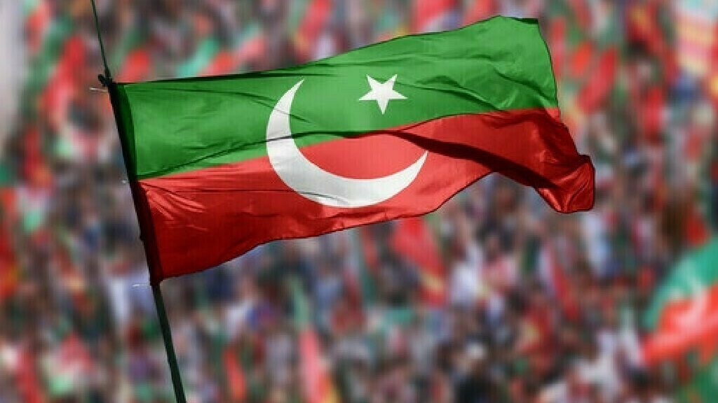 PTI flag featuring a green and red background with a white crescent and star, waving prominently in front of a large, blurred crowd, symbolizing political support and party identity amid claims of central government conspiracy.
