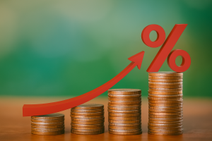 Stacks of coins increasing in height with a red upward arrow and percentage symbol, symbolizing rising financial pressure.