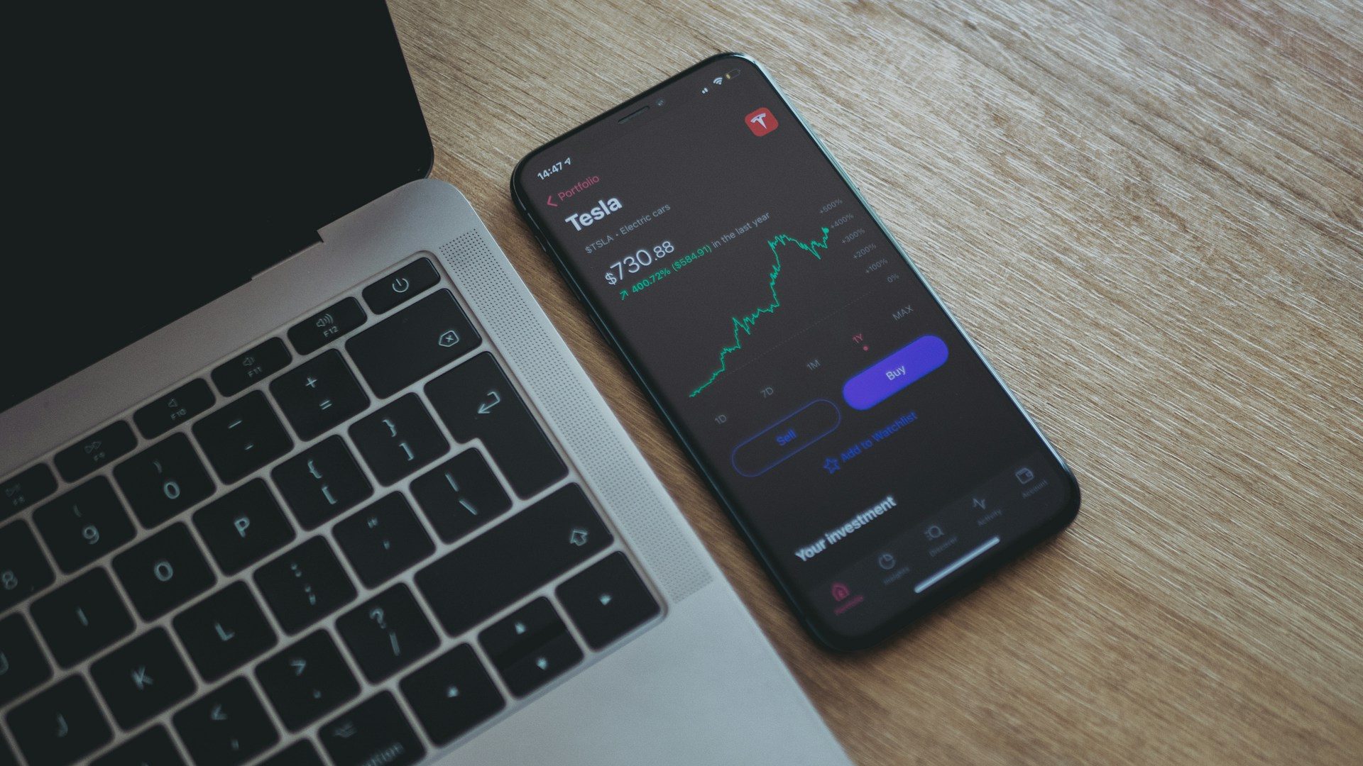 Pakistan Stock Market Surges on Iran-Israel Ceasefire – A smartphone displaying stock market data next to a laptop on a wooden desk, symbolising digital trading and investor activity.