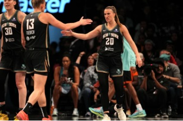Two women's basketball players exchange a high-five during a game, wearing black uniforms with “Team Stewart” on the front.