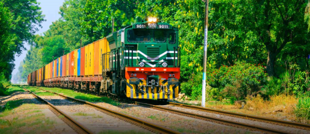 A green and red freight train travels through a snowy railway track under a cloudy sky, representing Pakistan’s first freight train to Russia from Lahore.