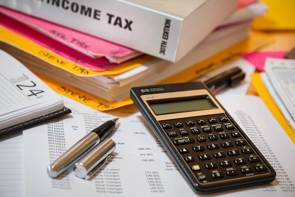 A calculator, pen, tax documents, and a binder labeled "Income Tax" lie on a cluttered desk—symbolizing financial concerns raised by taxation measures in Budget 2025-26.