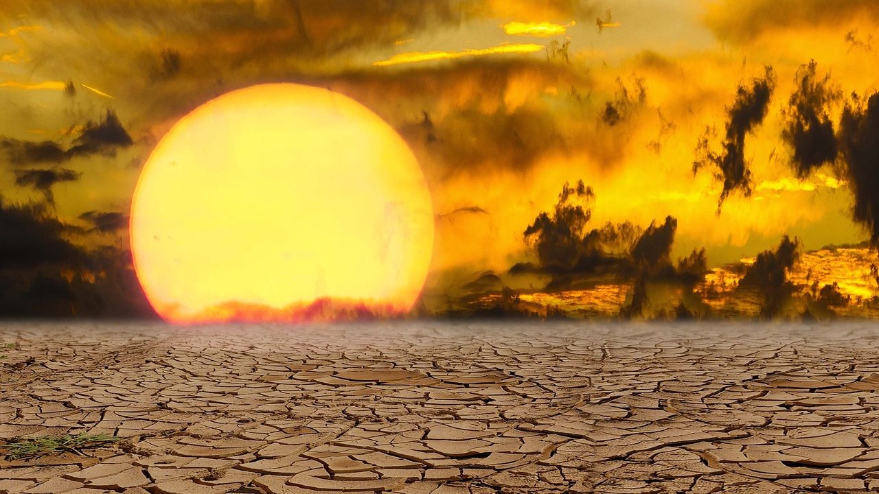 The image shows a dry, cracked earth landscape under a dramatic, fiery sky with a large sun setting or rising. It symbolizes extreme heat, drought, or climate change.
