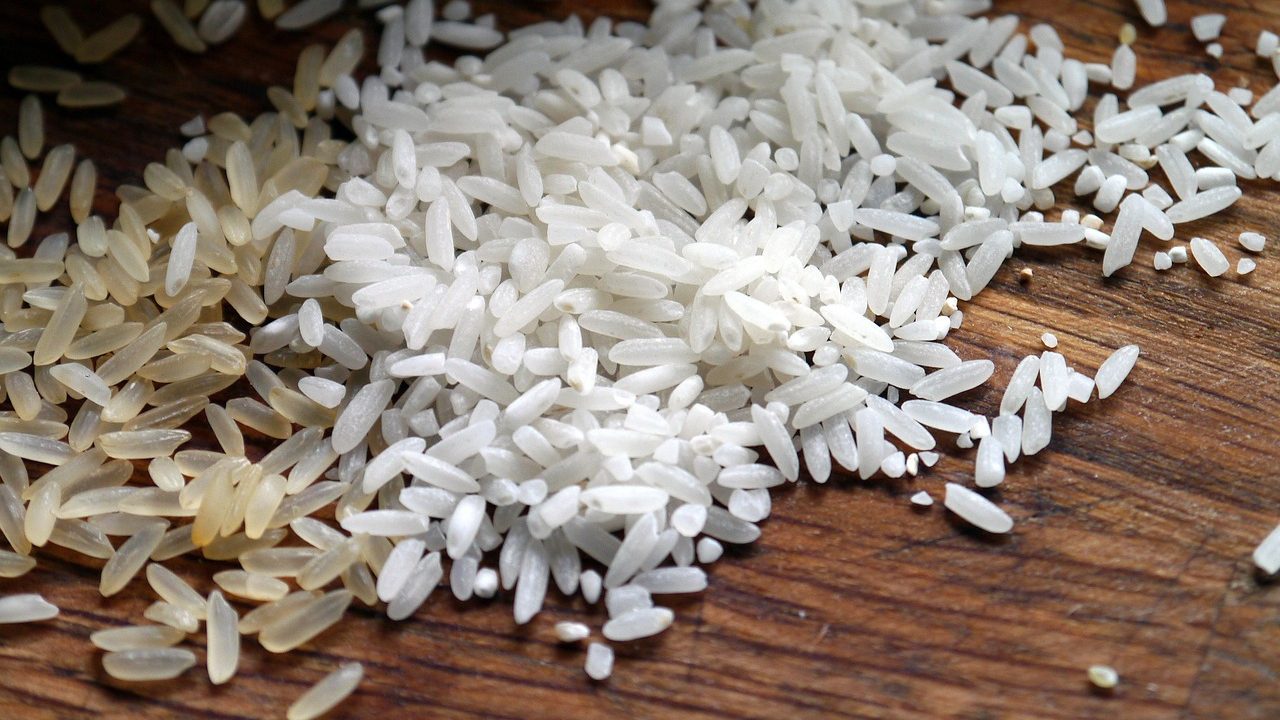 Close-up of two types of rice grains—parboiled and white—scattered on a wooden surface, symbolizing the resilience and quality of Pakistan's rice exports amid India's subsidized rice strategies.