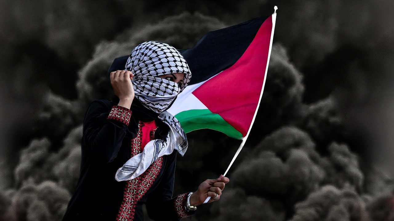 A woman wearing a traditional keffiyeh and embroidered dress holds the Palestinian flag against a backdrop of dark smoke — symbolizing resistance and unrest amid geopolitical tensions, in the context of Trump’s criticism of Israeli prosecutors over Netanyahu’s trial.
