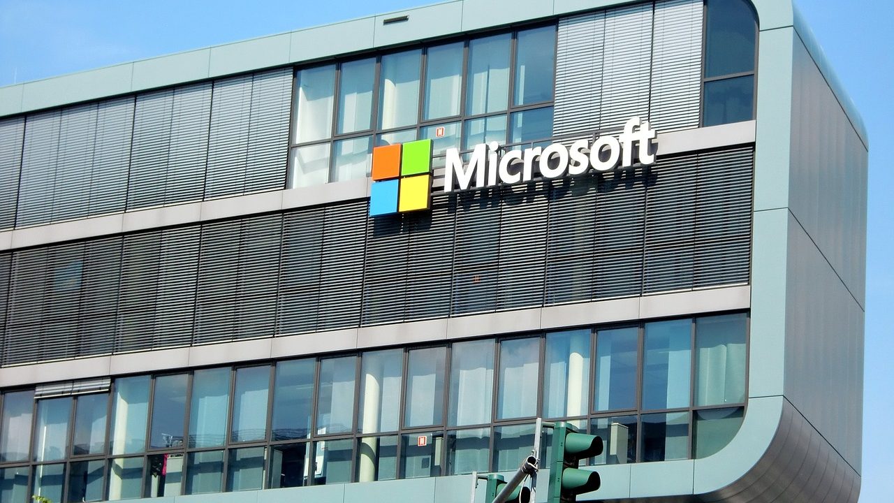 Microsoft Closes Office in Pakistan Amid Global Restructuring – A modern Microsoft office building with glass windows and the company logo, viewed from street level with a traffic light in the foreground.