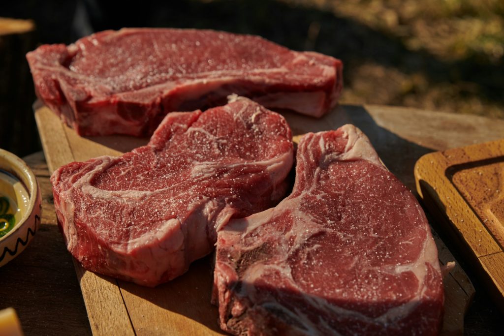 Raw beef steaks seasoned with salt, displayed on a wooden cutting board in outdoor natural light, highlighting the contrast between India's booming beef export industry and domestic cultural and religious sensitivities around beef consumption