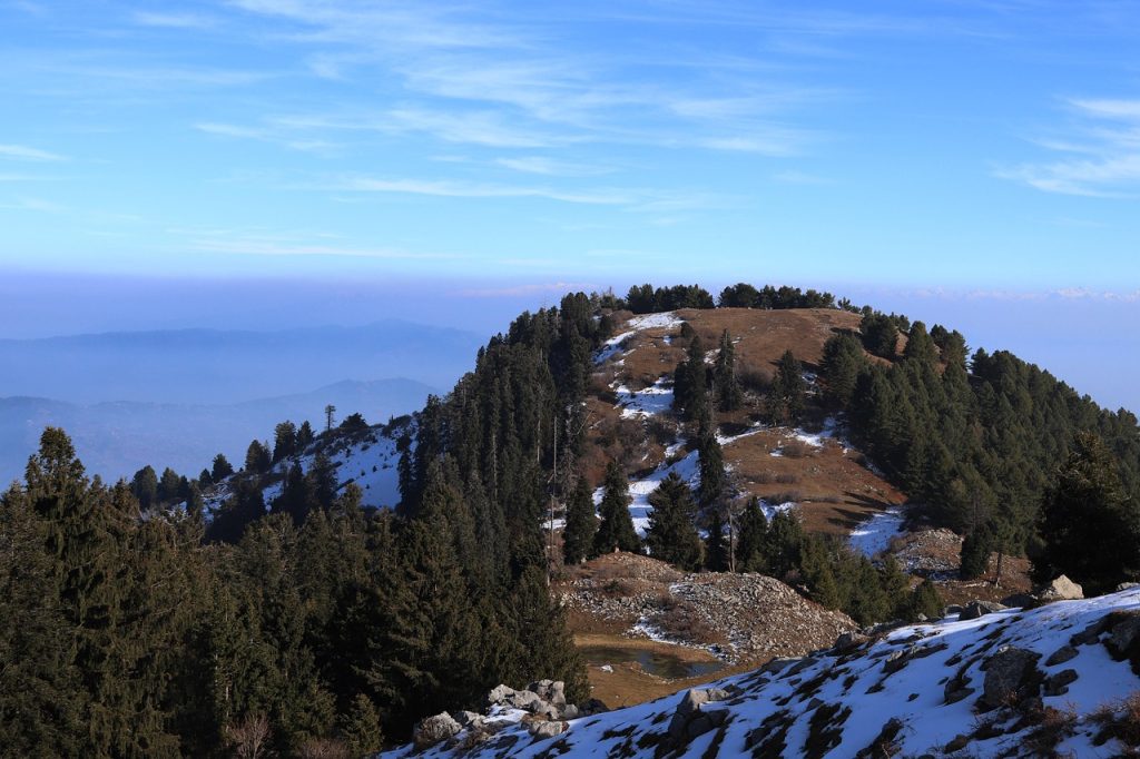Snow-dusted hills and pine-covered slopes at Mushkpuri Top in Murree, as drifting clouds and mysterious weather create a paradise-like atmosphere.