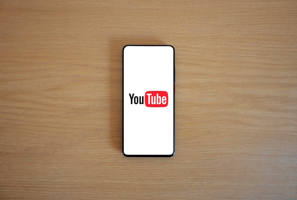 A smartphone displaying the YouTube logo on a white screen, placed on a wooden surface, symbolizing an upcoming major change to the platform's features.