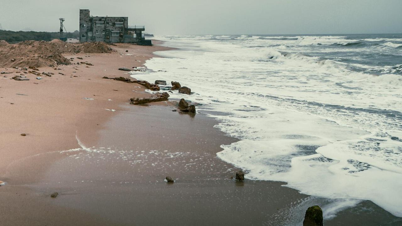 Hawke’s Bay Karachi: Cloudy beach with waves and an old building by the shore.