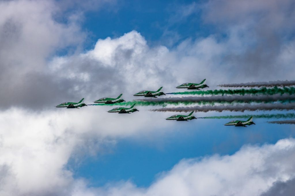 A formation of green-painted fighter jets from the Pakistan Air Force performs an aerial display with coloured smoke trails under a partly cloudy sky during the Royal International Air Tattoo.