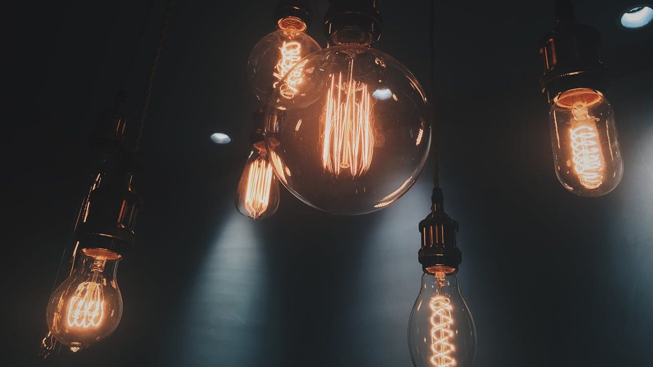 A group of vintage-style glowing filament light bulbs hanging in a dark room, symbolizing limited electricity use amid high prices and low consumption.