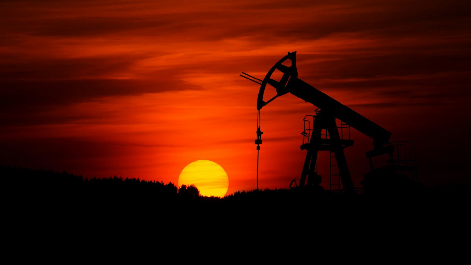 Silhouette of an oil pump jack operating at sunset, symbolizing global oil trade activities, with a fiery red sky in the background.